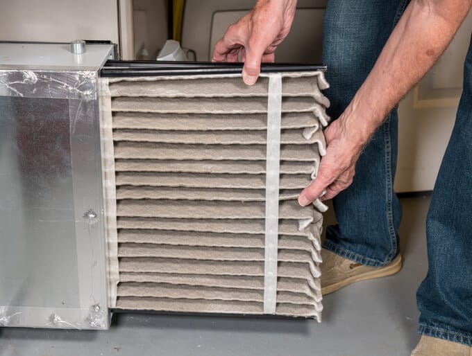  Repair man changing a folded dirty furnace air filter in the HVAC furnace system in basement of home