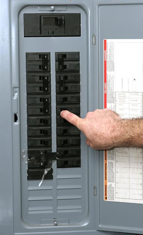 A closeup of an electrical panel with an electrician checking a tripped circuit breaker