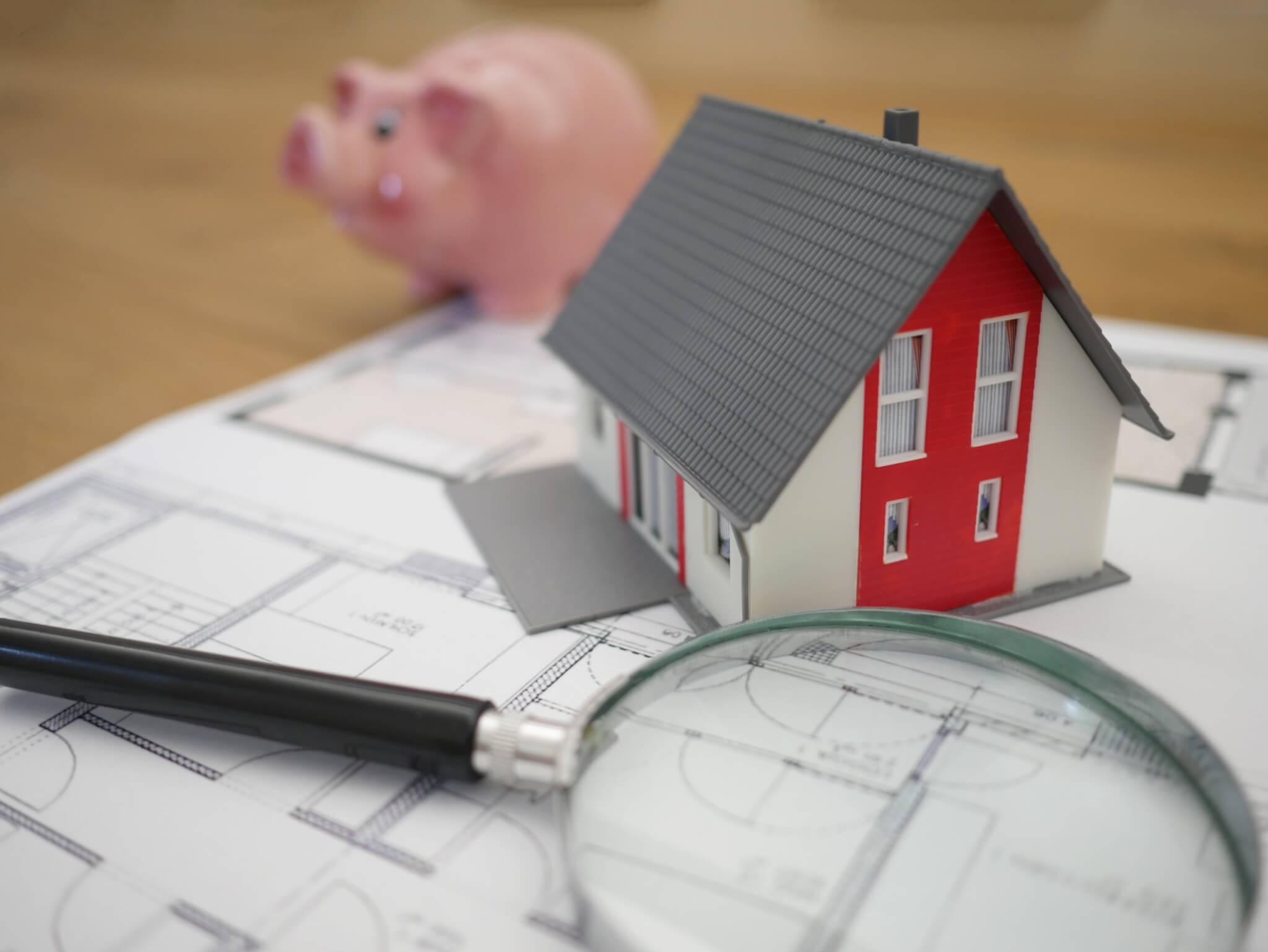 Model house next to magnifying glass and piggy bank on table