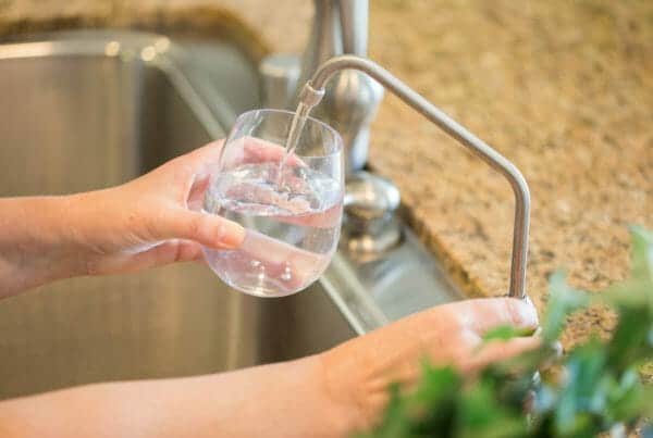 Woman Pouring Fresh Reverse Osmosis Purified Water Into Glass in Kitchen.