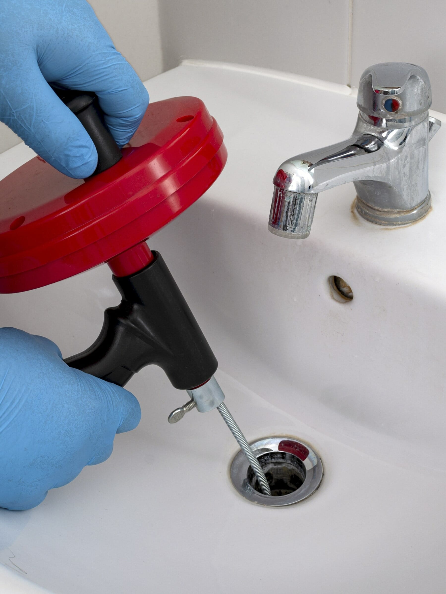 Hands with latex gloves use tools to clean drains
