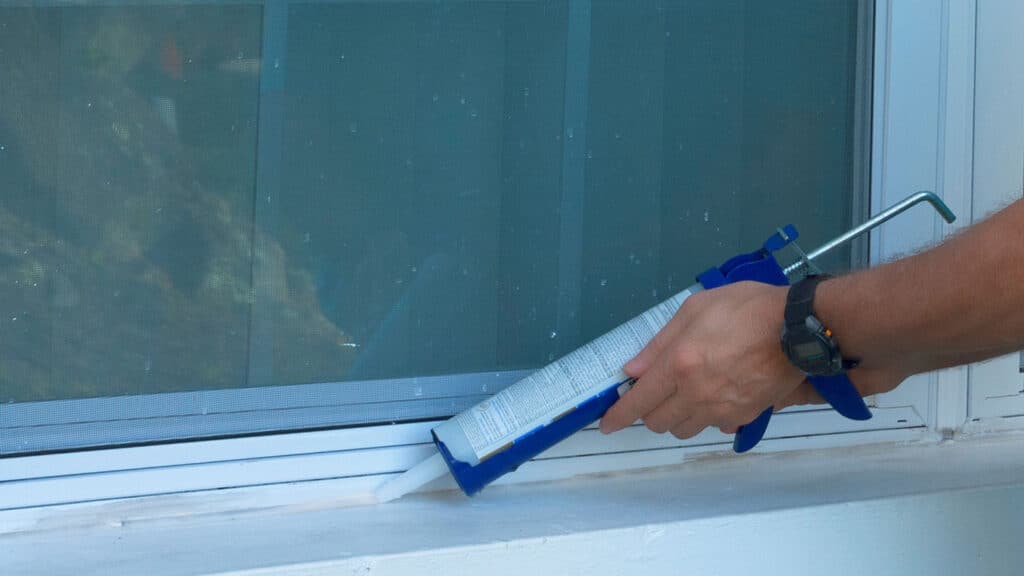 person caulks the outside of a window at their Utah home