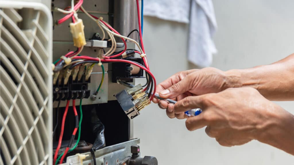 HVAC technician from Manwill using tools to repair a furnace control panel.