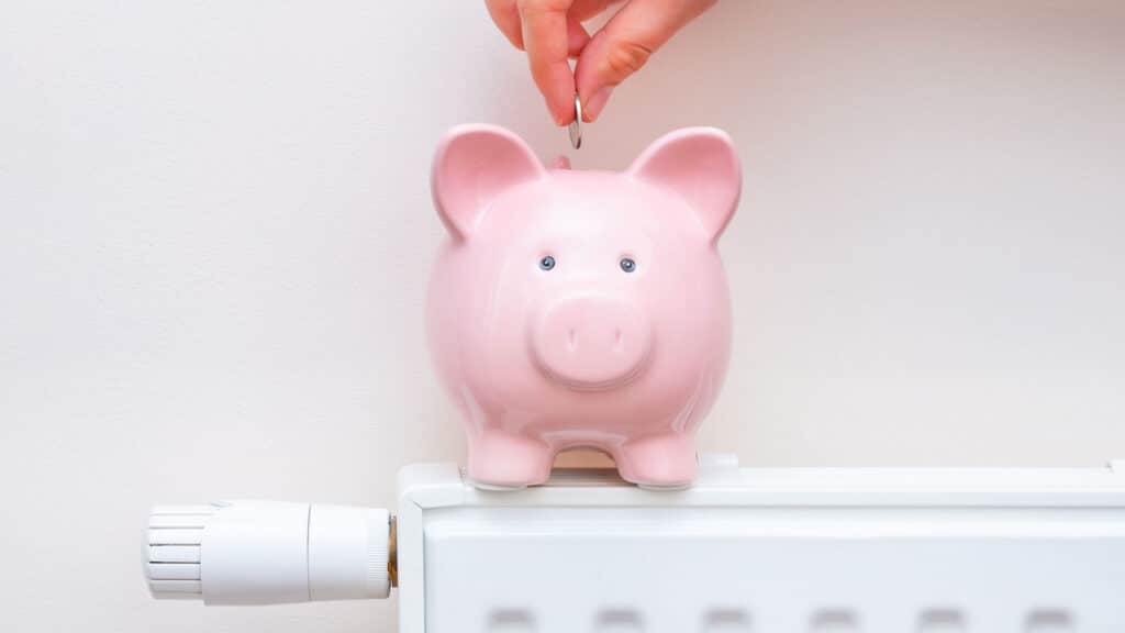 A person putting money in a piggy bank that is sitting on a heater.