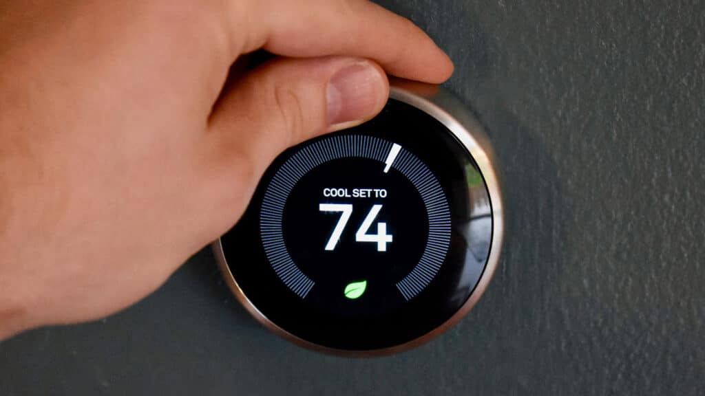 Person adjusting a digital thermostat to increase indoor temperature for energy efficient home heating service by Manwill technicians.