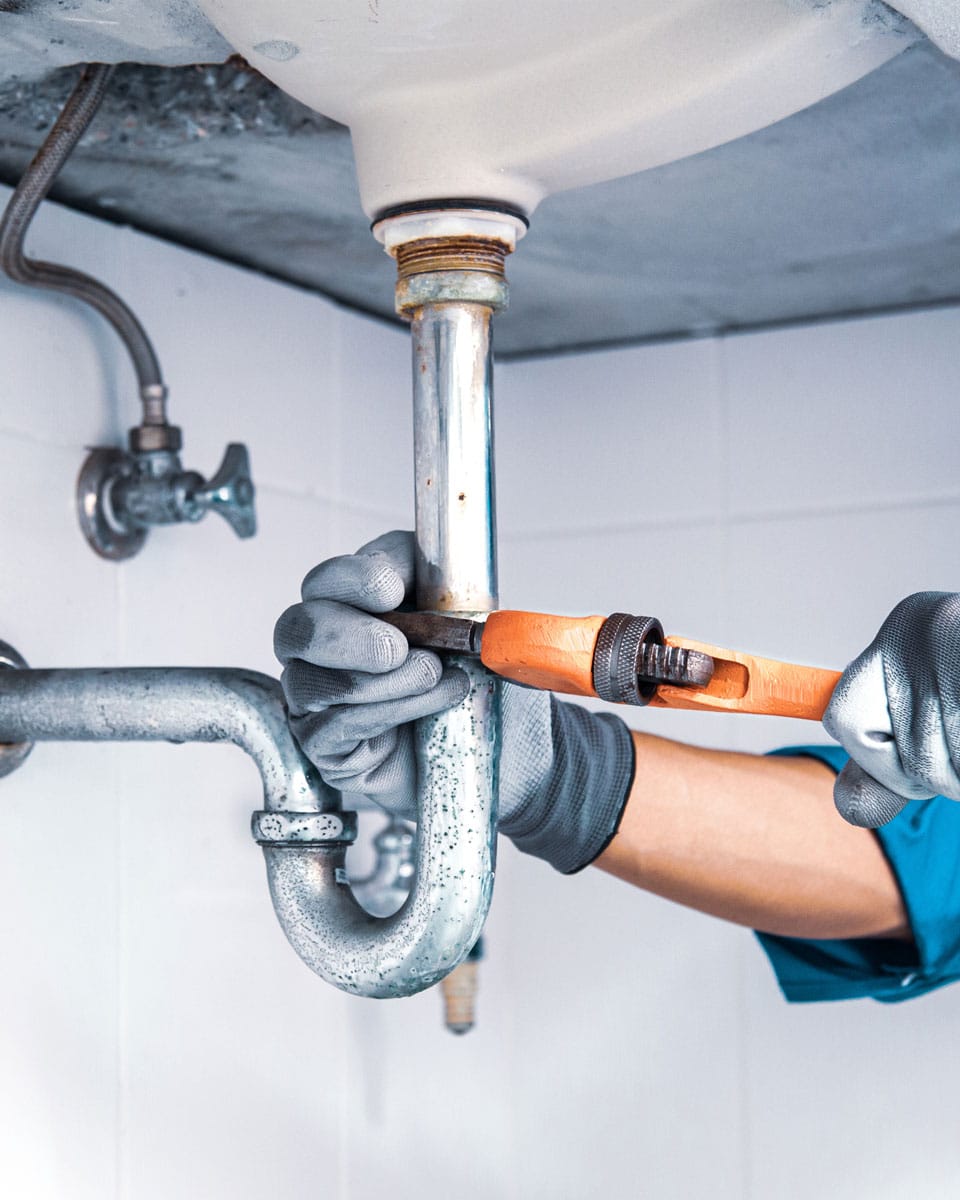 A plumber with a large wrench working on pipes under a sink during a plumbing repair appointment in Eagle Mountain.