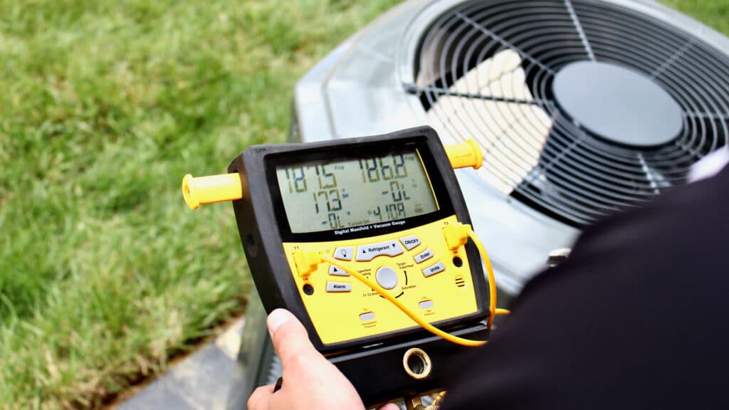 HVAC technician using a digital manifold gauge to check pressure on an outdoor air conditioning unit during routine maintenance