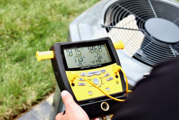 Close-up of a digital HVAC manifold gauge connected to an outdoor air conditioning condenser for maintenance and system diagnostics
