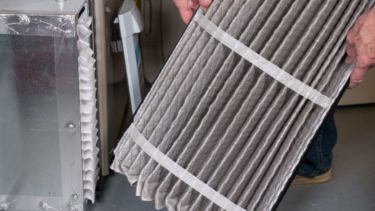 Dirty HVAC air filter being removed during air quality and furnace maintenance