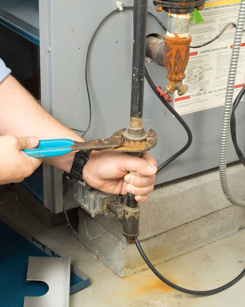 HVAC technician tightening a furnace gas-line connection during a heating repair