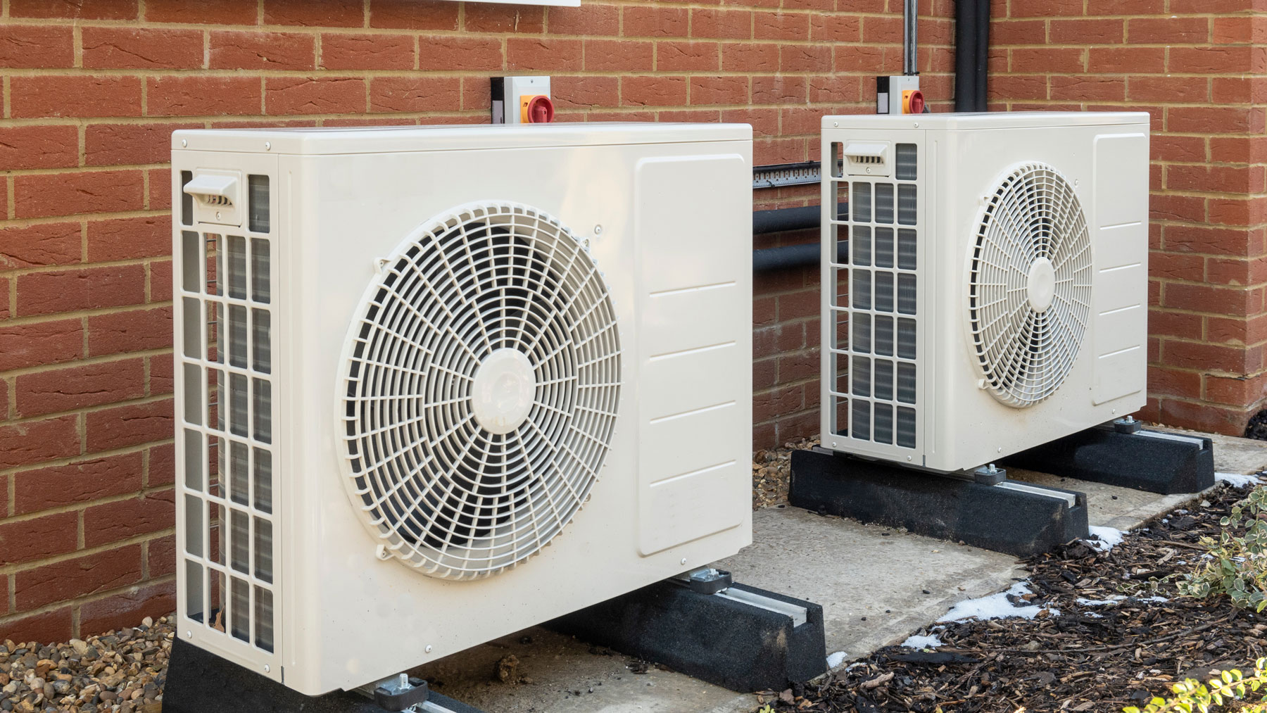 Two residential heat pump units installed outside a brick home